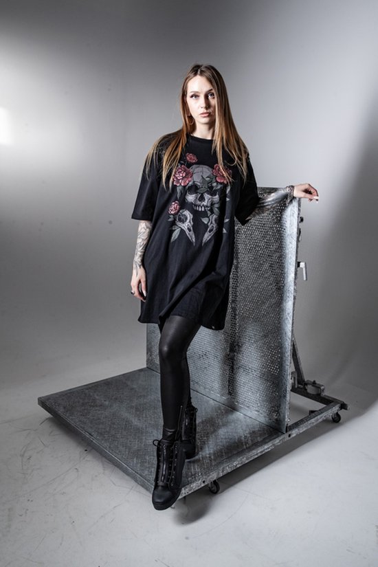 Vrouw met lang blond haar draagt een zwart oversized T-shirt met schedel- en rozenprint, leren legging en zwarte laarzen.