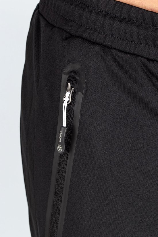 Detail van de rits van een zwarte trainingsbroek met merknaam 'SJENG'.