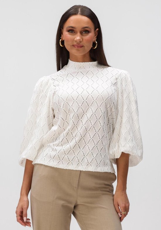 Model draagt een witte blouse met hoge hals, pofmouwen en opengewerkt ruitjespatroon. Gouden oorbellen.