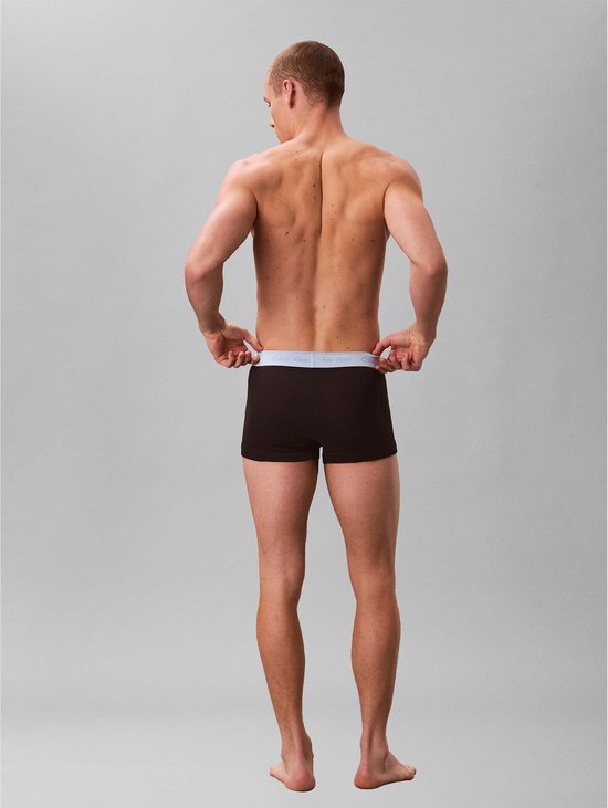 Man met bruine boxershorts met grijze Calvin Klein band, van achteren gezien.