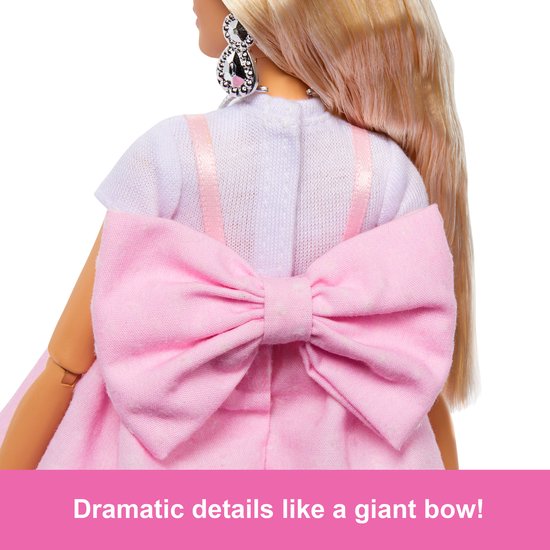 Barbiepop met grote roze strik op de rug van de jurk, een witte top en sprankelende oorbellen.