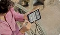 Vrouw met een roze gestreepte blouse houdt een auberginekleurige e-reader vast en schrijft erop met een stylus.