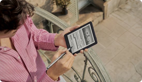 Vrouw met een roze gestreepte blouse houdt een auberginekleurige e-reader vast en schrijft erop met een stylus.