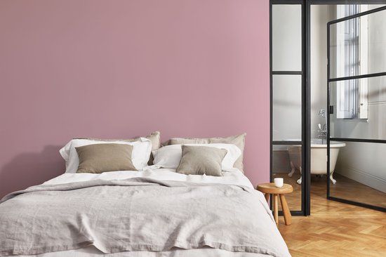 Slaapkamer met tweepersoonsbed en roze muur, naast een badkamer.