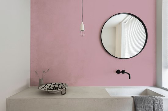 Badkamer met roze muur, betonnen wastafel en ronde spiegel.