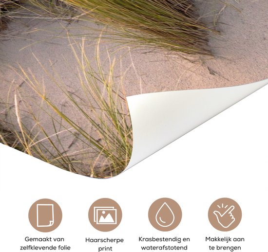 Detail van een zelfklevende deurposter met zand, duingras en een papieren laag die wordt losgetrokken.