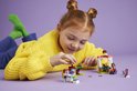 Fille aux couettes rousses et pull jaune jouant avec La Crêperie LEGO Friends sur fond violet.