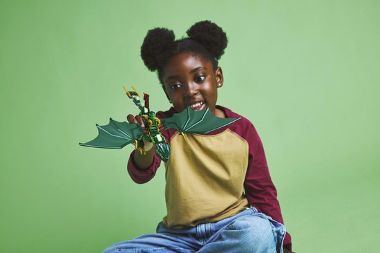 Jong meisje met afro-kapsel speelt met een groene LEGO draak met wijd gespreide vleugels.