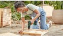 Vrouw met veiligheidsbril gebruikt groene Bosch accuboormachine om hout te schroeven.