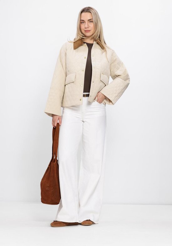 Vrouw in een gewatteerde crèmekleurige jas met bruine kraag, bruine top, witte wijde jeans en bruine tas.