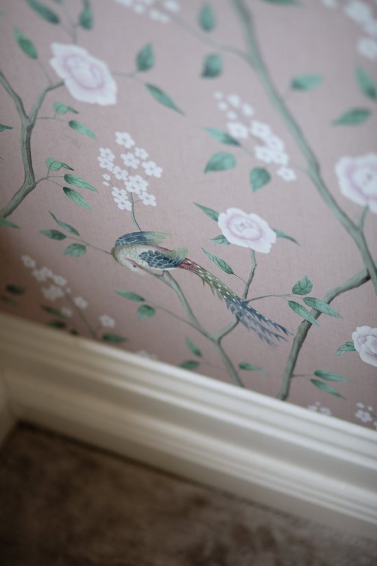 Roze behang met een patroon van takken, roze bloemen en een vogel.