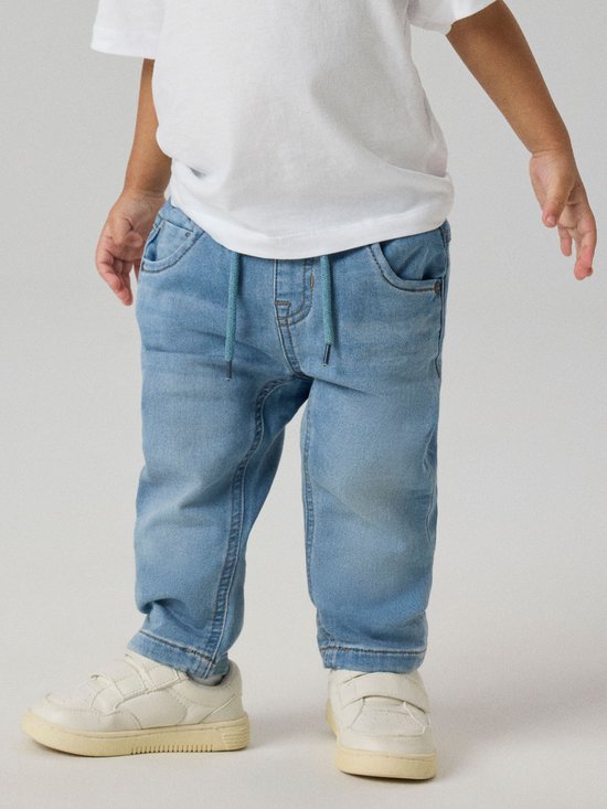 Jongen draagt een lichtblauwe spijkerbroek met trekkoord en witte sneakers.