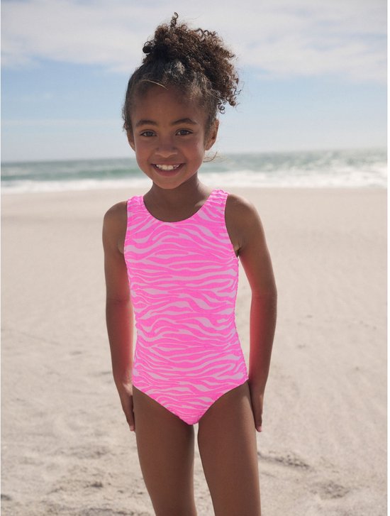 Meisje op het strand in een roze badpak met zebraprint, lachend.