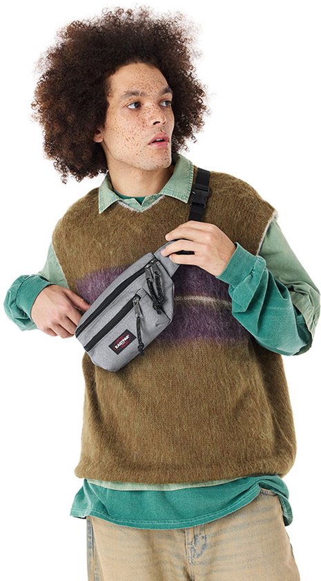 Sac banane Eastpak gris avec une bande violette et noire sur le devant, porté par un homme aux cheveux bouclés.
