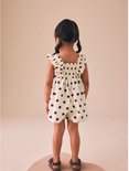 Meisje met staartjes, rug zichtbaar, draagt een crèmekleurige playsuit met bruine stippen.