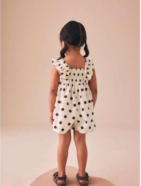 Meisje met staartjes, rug zichtbaar, draagt een crèmekleurige playsuit met bruine stippen.