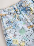 Detail van lichtblauwe spijkerbroek met all-over print van Smiley World-figuren, inclusief glimlachjes, bananen en tekst.
