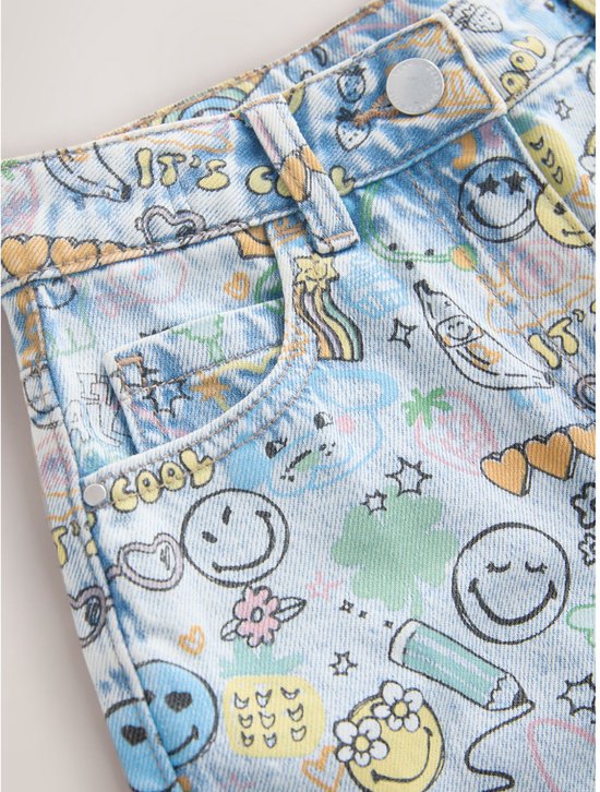 Detail van lichtblauwe spijkerbroek met all-over print van Smiley World-figuren, inclusief glimlachjes, bananen en tekst.