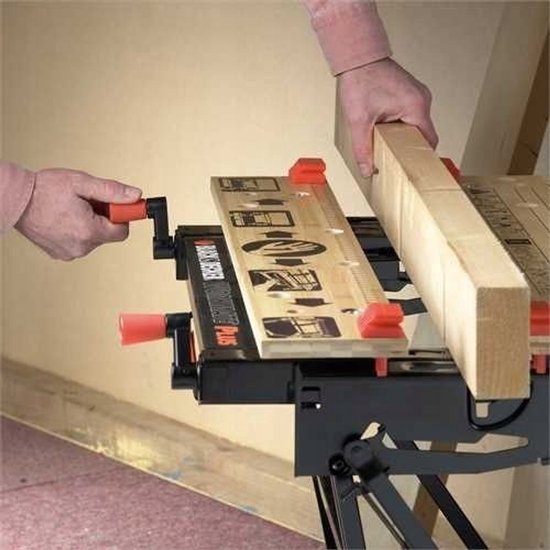 Een hand met een oranje handvat draait aan de werkbank, terwijl een andere hand een houten plank vasthoudt.
