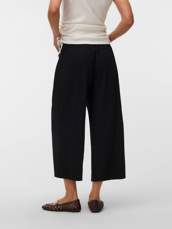 Zijaanzicht van een zwangere vrouw in witte top en zwarte, wijde, cropped zwangerschapsbroek.