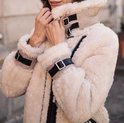 Femme aux longues boucles brunes, porte une veste en shearling crème avec des détails en cuir noir comme des boucles au col et aux poignets.