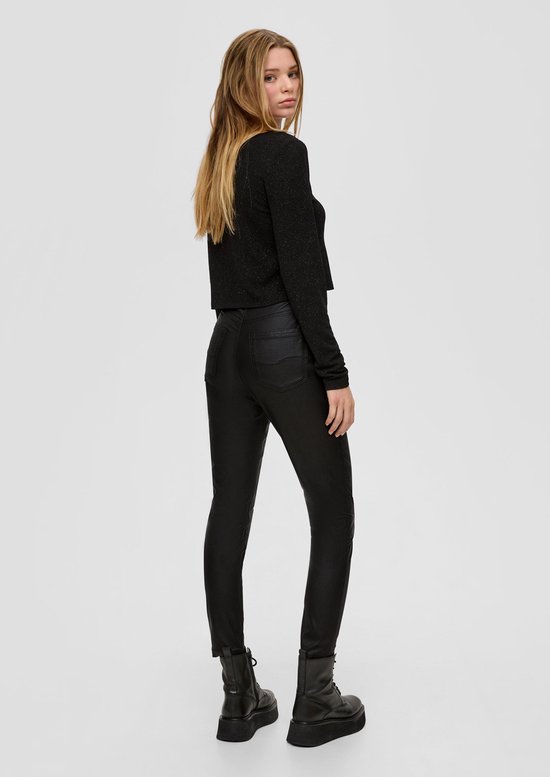 Model op de rug gezien, draagt zwarte broek met coating en zwarte veterlaarzen met dikke zool.