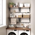 Wandkapstok met houten planken, kledingstangen en haken, boven wasmachines.