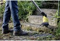 Man in spijkerbroek gebruikt de gele en zwarte voegenborstel op stenen trappen.