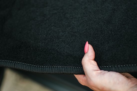 Vrouwenhand met roze nagellak raakt de rand van een zwarte vloermat aan.