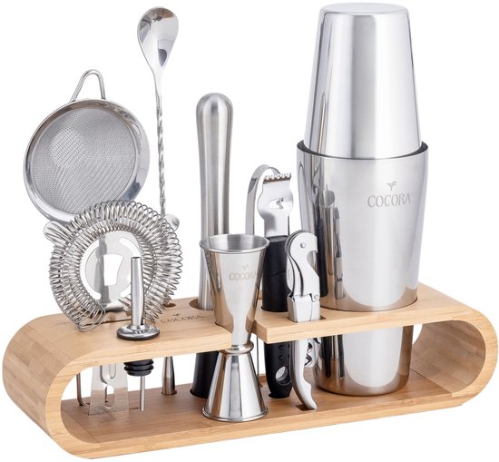 Zilverkleurige cocktailset met Boston shaker, zeef, jigger en barlepel op een houten standaard.
