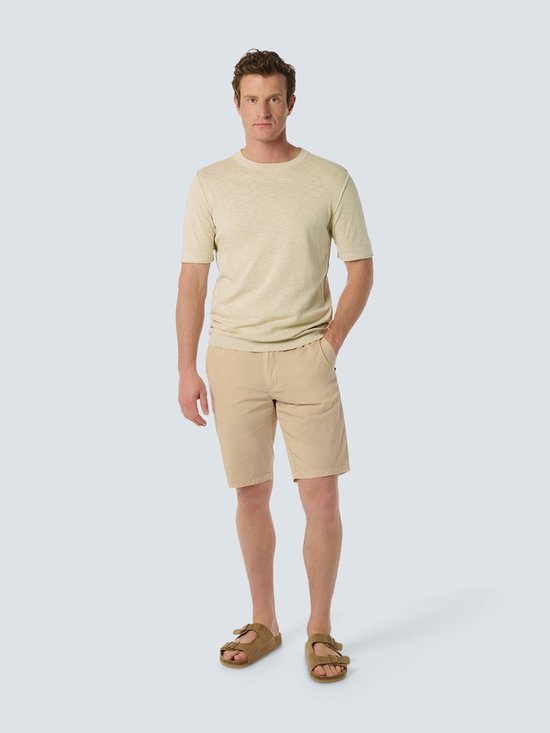 Homme portant un haut beige à manches courtes et un short beige.