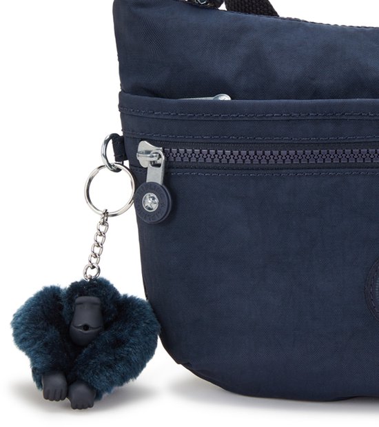 Detail van een donkerblauwe Kipling schoudertas met een harige aap sleutelhanger.