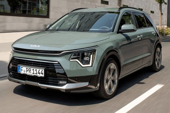 Een lichtgroene Kia Niro rijdt over een straat, de voorkant is duidelijk zichtbaar.