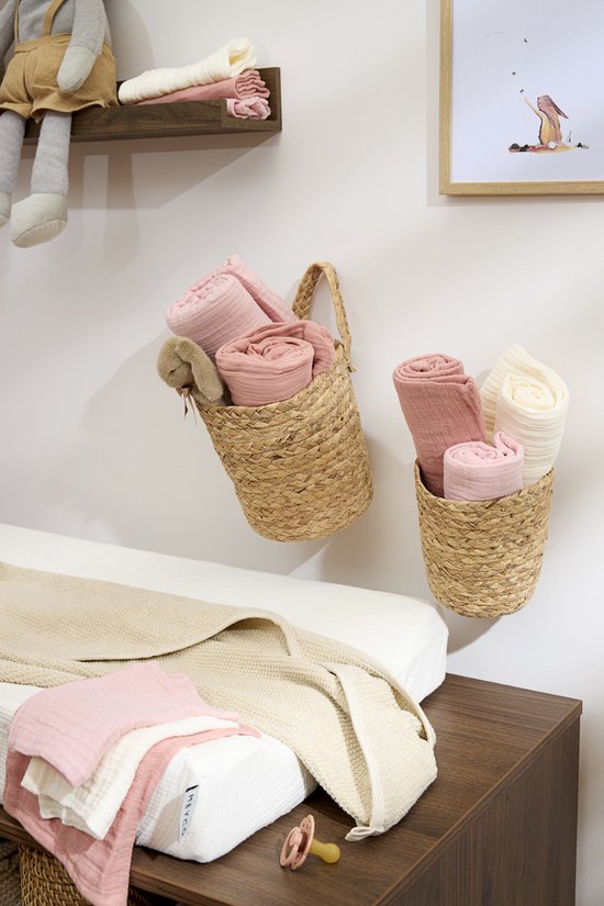 Babykamer met opgerolde zachtroze en crèmekleurige hydrofiele doeken in manden en op een commode.