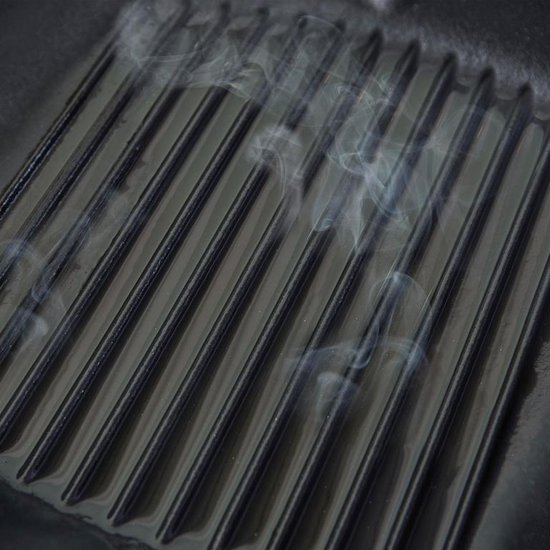 Gietijzeren grillpan met zwarte ribbels en rookontwikkeling.