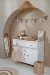 Kinderkamer met witte commode, rotan aankleedmand, babykleding en decoraties.