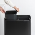 Gros plan du dessus d'une poubelle Brabantia noire. Deux mains retirent une poubelle intérieure grise.