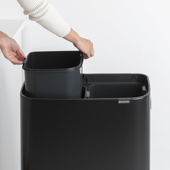 Gros plan du dessus d'une poubelle Brabantia noire. Deux mains retirent une poubelle intérieure grise.