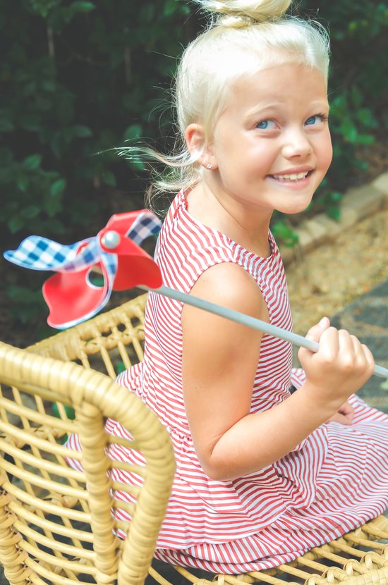 Meisje met blond haar in een gestreepte jurk, vasthoudend aan een rood-wit-blauw windmolentje.