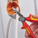 Hand gebruikt rode en gele tang om een witte kabel te strippen in een oranje doos.
