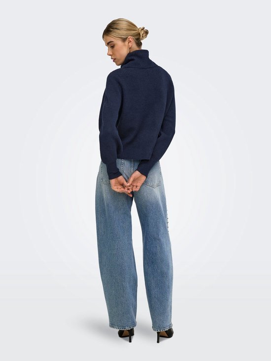 Model van achteren met een marineblauwe coltrui en een wijde spijkerbroek.