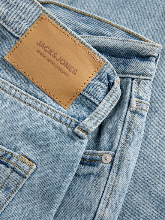 Detail van een lichtblauwe spijkerbroek met een bruin lederen label met de tekst 'JACK & JONES JEANS INTELLIGENCE'.