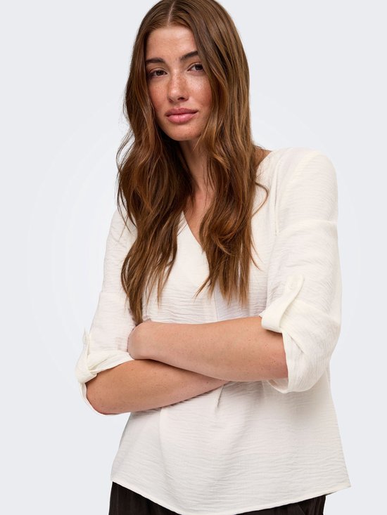 Close-up van model in witte blouse met kreuktextuur, armen over elkaar.