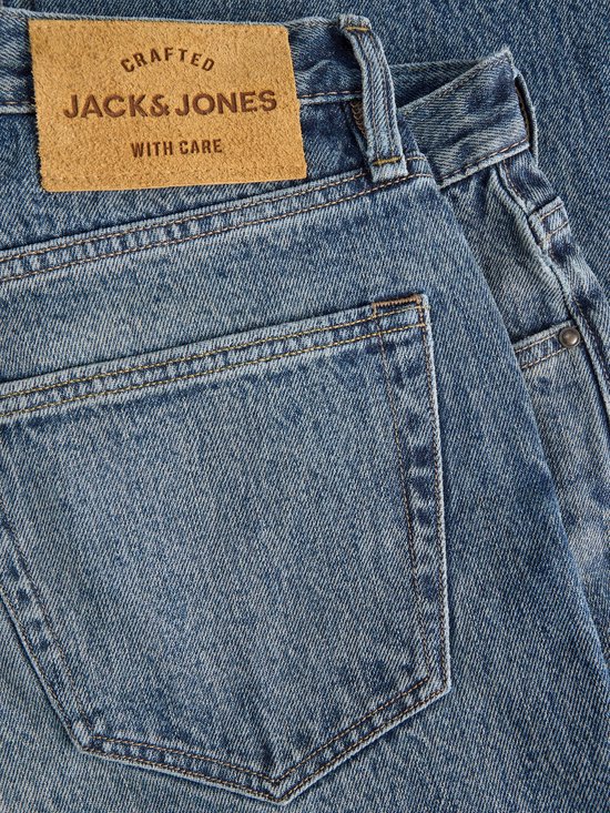 Close-up van de achterkant van een spijkerbroek met een bruin leren label met 'CRAFTED JACK & JONES WITH CARE'.