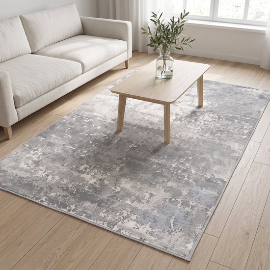 Grijs vloerkleed met abstract patroon op een houten vloer, naast een witte bank.