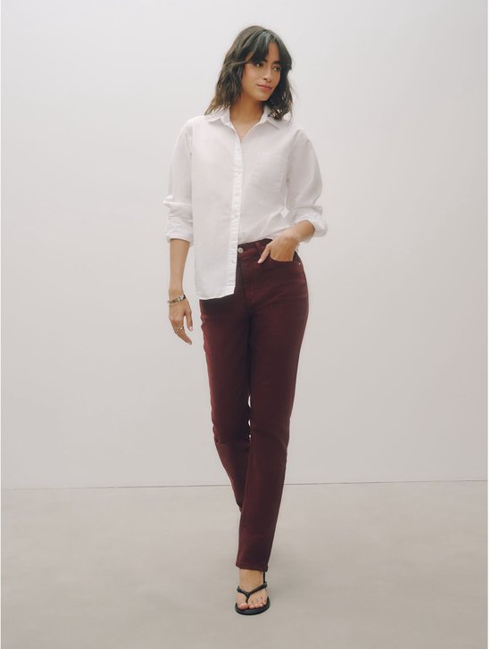 Staand model draagt een donkerrode slim-fit stretchjeans met halfhoge taille en een wit overhemd.
