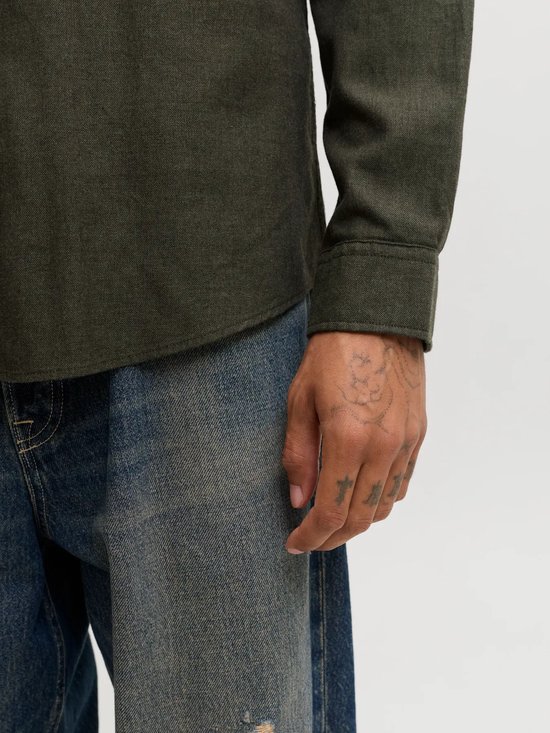 Detailopname van de mouwmanchet van een donkergroen overhemd op een getatoeëerde hand.