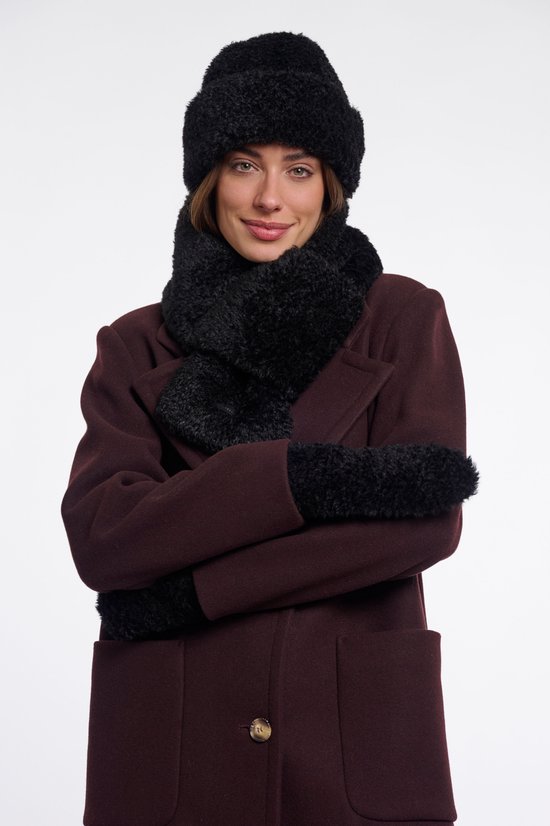 Model met gekruiste armen, draagt een zwarte set van muts, sjaal en handschoenen van imitatiebont bij een bordeauxrode jas.