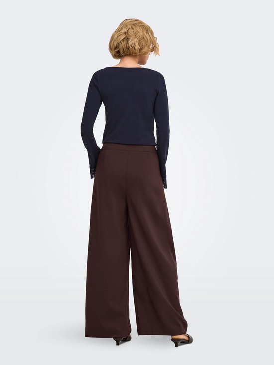 Achterkant van bruine wijde broek met plooien, gecombineerd met een donkerblauw shirt met kanten details.