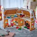 Een open LEGO peperkoekhuisje met een kerstman met een zak. Binnen zijn een bed, keuken, piano en een bureau te zien.